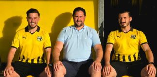 Three men posing on a yellow bench; two wear yellow soccer jerseys with FCE crest, one in a light blue polo in the middle.