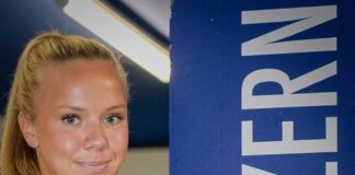 Smiling young woman with blonde hair in a blue shirt stands beside a tall blue column that reads 'LUZERN' vertically.