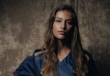 FCL: Drei Neuzugänge im AWSL-Team Young woman with long hair in a blue soccer jersey, holding a leather ball against a textured gray backdrop.