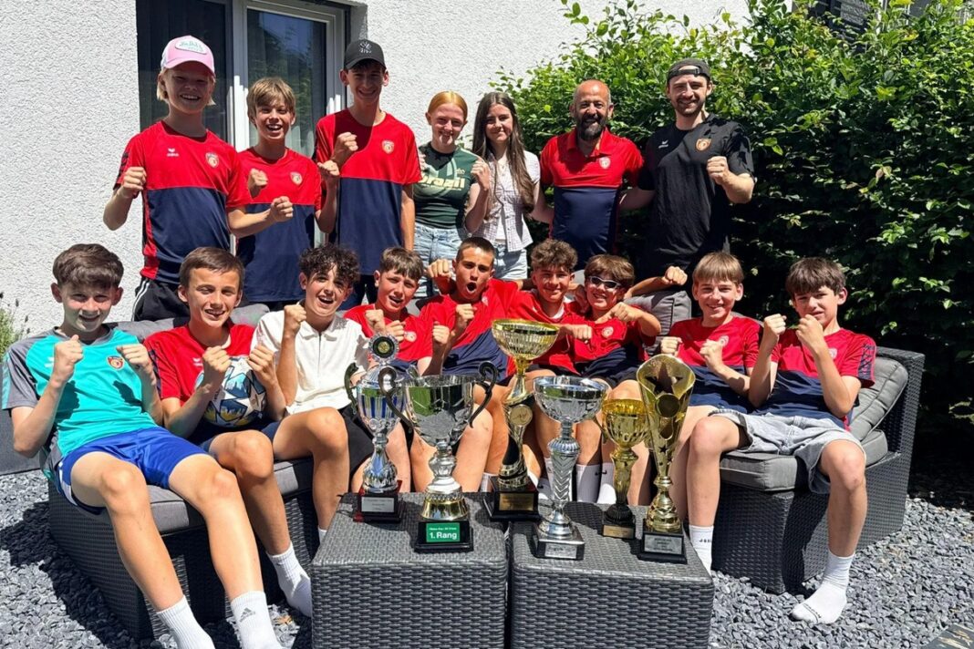 scchamda Young soccer team posing with trophies on outdoor seating, fists raised in celebration after a tournament win.