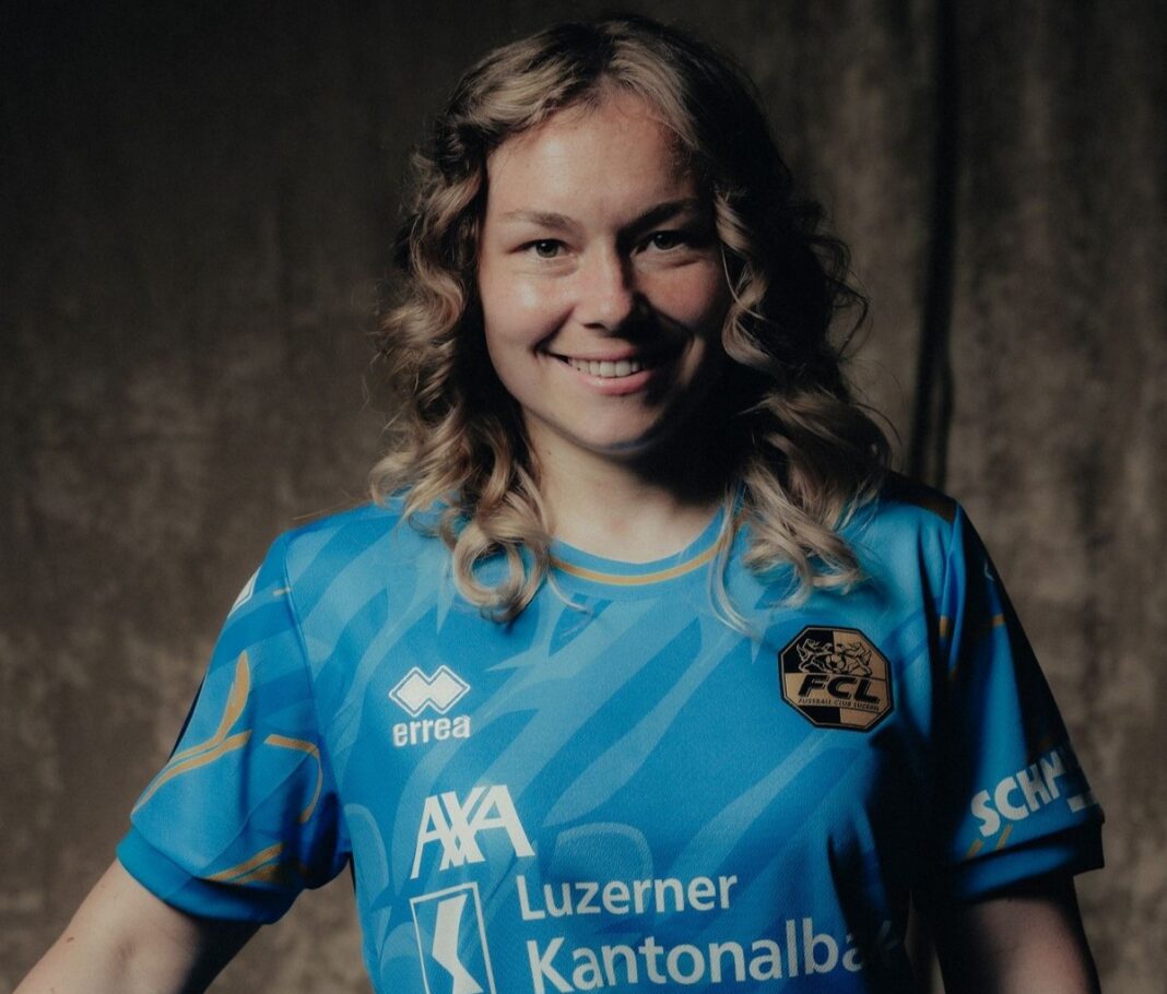 vogt-laura-awsl Smiling woman in a blue sports jersey with logos, posed against a dark backdrop.