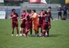Torreiches Testspiel: Perlen-Buchrain und Emmen trennen sich 3:3 Group of soccer players in maroon uniforms huddle and high-five on a sunny green field, with an orange-clad goalkeeper nearby.