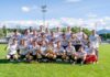 Neue Gesichter, neue Wege: Die 4. Liga startet in sechs Gruppen Group of soccer players in white jerseys posing for a victory photo on a sunny field, holding a trophy.