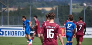 Soccer players on a field, maroon team with number 16 foreground watching a game against blue team in the background