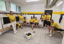 FC Emmenbrücke im Umbruch: Bereit für die nächste Herausforderung Group of men in yellow and black jerseys gather in a locker room, some sitting on benches and others leaning against the wall.
