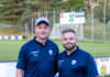 FC Littau verpflichtet neuen Assistenz- und Torhütertrainer Two coaches in matching navy polo shirts stand together on a grassy soccer field, smiling at the camera with a goal and banners in the background.