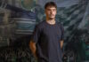 Elio Rufener wechselt von YB in die Zentralschweiz Portrait of a young man in a dark T-shirt standing in front of a green-and-white sports banner backdrop.