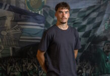Elio Rufener wechselt von YB in die Zentralschweiz Portrait of a young man in a dark T-shirt standing in front of a green-and-white sports banner backdrop.