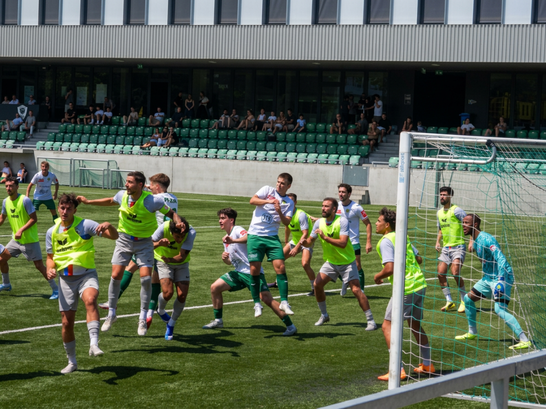 Firefly_Gemini Flash_Das bild noch qualitativ stark verbessern und auch die Beleuchtung ausgewogen umsetze 524718 Soccer players in neon vests collide near the goal while a goalkeeper in turquoise watches from the right, in a stadium with green seats and spectators in the background.