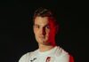 FC Hergiswil stellt Staff der Aktivmannschaften für die neue Saison auf Portrait of a man in a white sports jersey with a crest, facing the camera against a dark background.