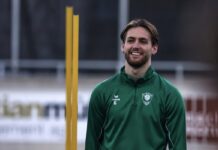 SC Kriens: Leandro Aversa verlängert und wechselt Smiling man in a green training jacket with number 6 stands on a sports field, orange training posts in the background.