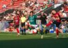 Später Sturmlauf bleibt unbelohnt: Kriens verpasst Punktgewinn knapp Soccer match action: green player and red-black player contest a high ball near the sideline with a crowd in the stands behind them.