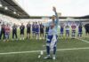 FCL: Andrej Vasovic wechselt zu Club Brügge Soccer players in blue kits stand in a line on the field applauding as a teammate raises his right hand in celebration at the stadium edge.