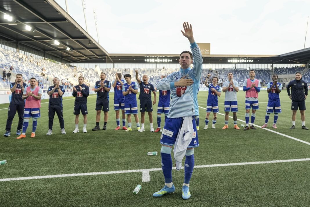 LAUSANNE - LUZERN Soccer players in blue kits stand in a line on the field applauding as a teammate raises his right hand in celebration at the stadium edge.