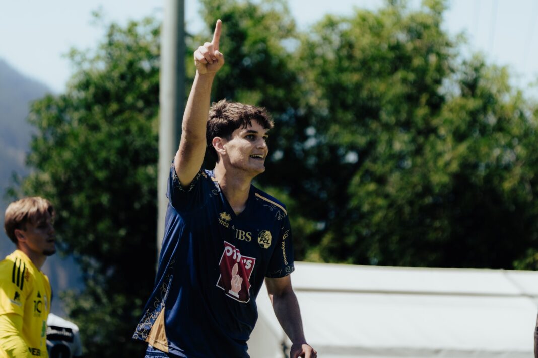 Young man in a blue sports jersey raises his index finger in celebration outdoors during a game.