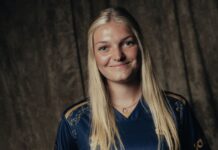 FCL: Romy Baraniak stösst zum AWSL-Team Smiling young woman with long blonde hair wearing a navy sports jersey, standing against a dark textured backdrop.