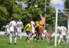 Stirbt die Kategorie der A-Junioren auch im IFV-Gebiet aus? Soccer game near the goal with an orange-clad goalkeeper jumping to punch the ball away amid white and yellow players nearby.