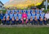Neue Gesichter, neue Derbys: Die 5. Liga ist eingeteilt Group of soccer players in blue-and-white striped uniforms posing on concrete steps with a pink-clad goalkeeper holding a ball; coaches flank them, rural field backdrop behind.