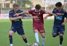 FC Luzern U21 mit geglückter Hauptprobe Three soccer players in blue and maroon kits compete for the ball on a green field during a match, with the central maroon player shielding the ball from two opponents.