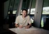 FC Luzern: Levin Winkler verlängert vorzeitig bis 2029 Man sits at a marble table signing a document with a pen in a bright, modern room with large windows behind him and daylight coming in.