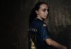 FCL: Michelle Gigante stösst zum AWSL-Team Portrait of a person in a blue and gold sports jersey, turned to look over their shoulder against a dark textured background.