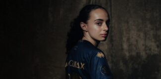 Portrait of a person in a blue and gold sports jersey, turned to look over their shoulder against a dark textured background.