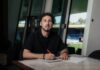 FCL: Ronaldo Dantas Fernandes verlängert vorzeitig Man with curly dark hair and beard sits at a marble table, signing papers with a red pen indoors by large windows.