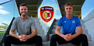 Two athletes sit on concrete stadium steps with hands clasped, SC Cham crest centered between them behind.