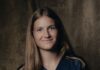 Valentina Gerlof wechselt leihweise zum Luzerner AWSL-Team Portrait of a young woman with long brown hair smiling at the camera, wearing a navy top with a pendant necklace, against a dark studio backdrop.