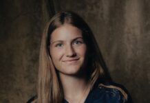 Valentina Gerlof wechselt leihweise zum Luzerner AWSL-Team Portrait of a young woman with long brown hair smiling at the camera, wearing a navy top with a pendant necklace, against a dark studio backdrop.