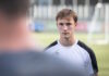 SC Kriens verstärkt die Offensive Portrait of a young male athlete in a white and black jersey, facing the camera on a grassy soccer field with a blurred teammate in the foreground.