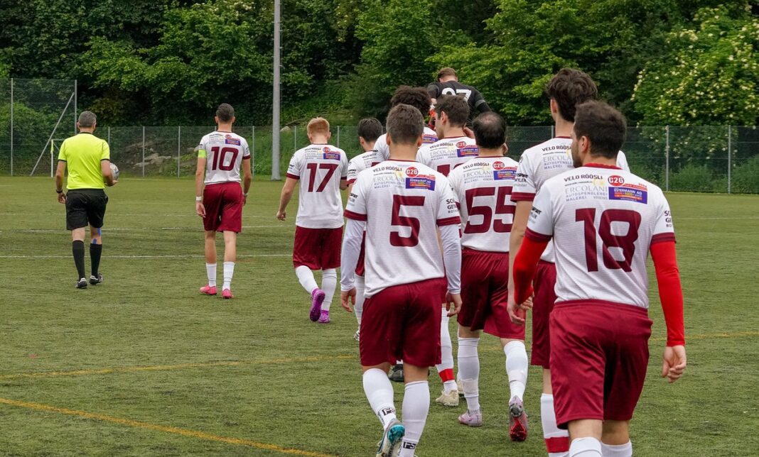 Soccer players in white and maroon uniforms walk onto the field from the back, heading toward play.