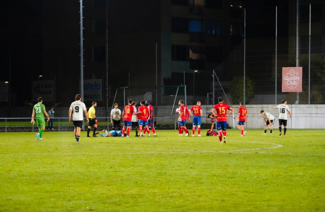 784426812_28401462846117093_1392730722947973588_n Nighttime soccer match with players in red and white; a group clusters around a fallen teammate on the green field.