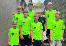 FC Gunzwil: Fussball, Schweiss und viel Teamgeist in Bad Ragaz Seven young boys in neon green soccer jerseys posing together on a concrete stairwell outdoors, smiling at the camera.