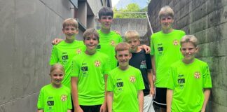 Seven young boys in neon green soccer jerseys posing together on a concrete stairwell outdoors, smiling at the camera.