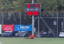 FC Gunzwil: Später Lucky-Punch zum Erfolg beim SC OG Soccer field with scoreboard showing 3–4 and 90:00; player in orange sits on the turf near banners.