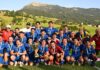 FC Küssnacht startet mit Zuversicht in die neue 2.-Liga-Saison Group of men in blue soccer uniforms posing with a large trophy and medals on a sunny grassy field, hills and mountains in the background.
