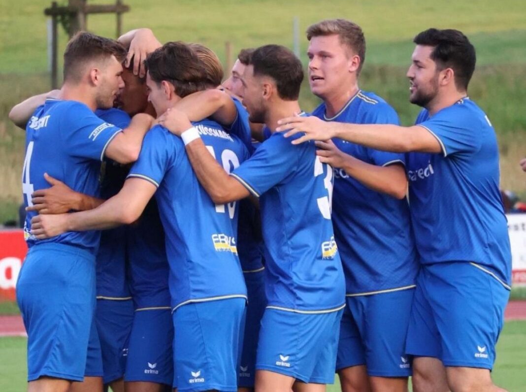 Bildquelle-IFV Soccer players in blue jerseys form a huddle, arms around each other in celebration on a field