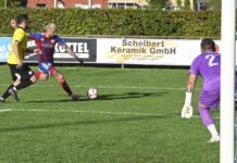 Zwei Standartsituationen entscheiden Duell Brunnen gegen Emmenbrücke Soccer scene: a player in blue and red striped kit kicks the ball while a yellow-jersey opponent approaches on a grassy field, with a purple-clad goalkeeper near the goal in the background