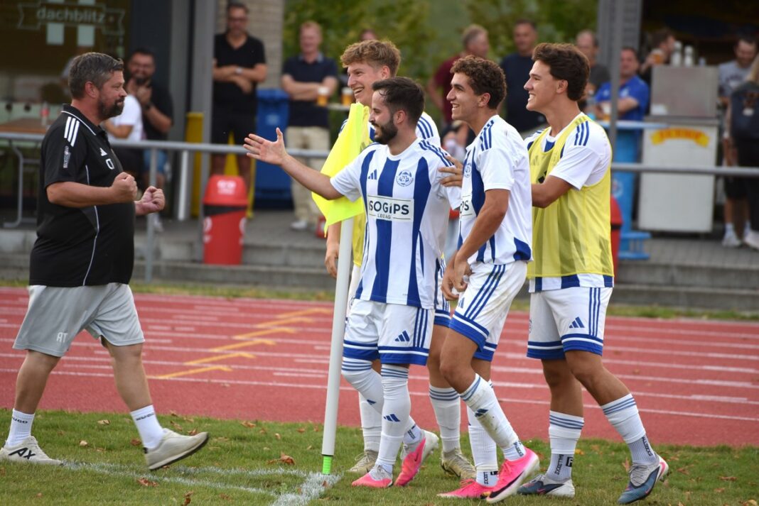 Soccer players in white and blue striped kits celebrate near the sideline, gesturing and smiling at a coach