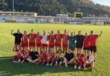 Die FC Küssnacht Frauen ziehen souverän in die zweite Cuprunde ein Group of female soccer players in red uniforms pose together on a grassy field after a match, some with fists raised in celebration, wearing medals.",