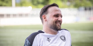 Smiling man with short dark hair and beard on a soccer field, wearing a white jersey with a club crest and the number 9.