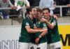 Kriens übersteht schwierige Startphase und schlägt Nyon klar Three soccer teammates in green jerseys celebrate a goal together on the field, arms around each other, smiles on their faces in front of a stadium crowd.