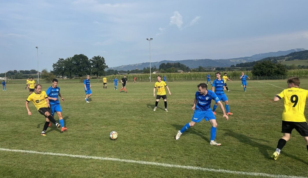 Spielszene Cup-Partie Dietwil gegen Grosswangen-Ettiswil Soccer match on a sunny field with players in yellow and blue contesting the ball, hills in the background.