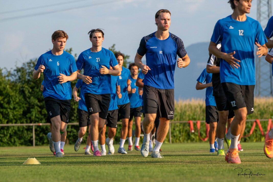Trainingsstart Cham II-3 Group of male soccer players in blue jerseys running on a grassy training field.