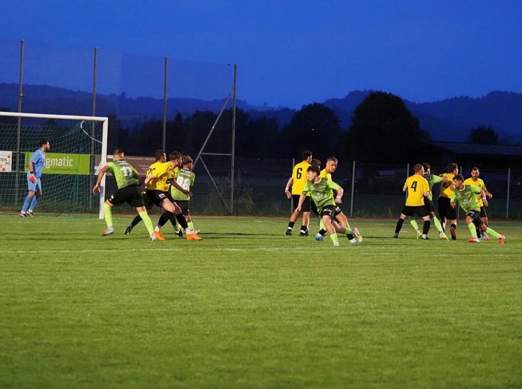 Vorbereitungsspiel gegen den FC Emmenbrücke Soccer match at dusk with players in green and yellow near the goal and a blue-clad goalkeeper watching the action.