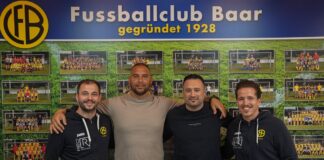 Four men stand arm-in-arm in front of a FC Baar photo wall; banner reads 'Fussballclub Baar gegründet 1928'