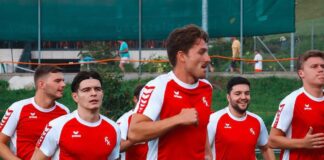 A group of young men in red and white soccer jerseys jogging together on a track field.