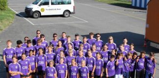 Group of children and teens in purple CSS jerseys posing for a team photo in a parking lot beside a white van with a club logo.