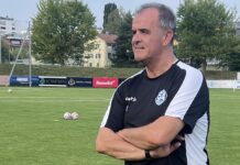 Erminio Piserchia: «Wir wollen agieren statt reagieren» Coach on a soccer field with arms crossed, wearing a black and white training shirt (number 94) and banners in the background.